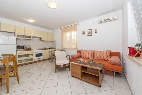 A compact living space with a kitchenette, a sofa with cushions, a coffee table, and a dining area with chairs. - Apartment Katarina (Zadar)