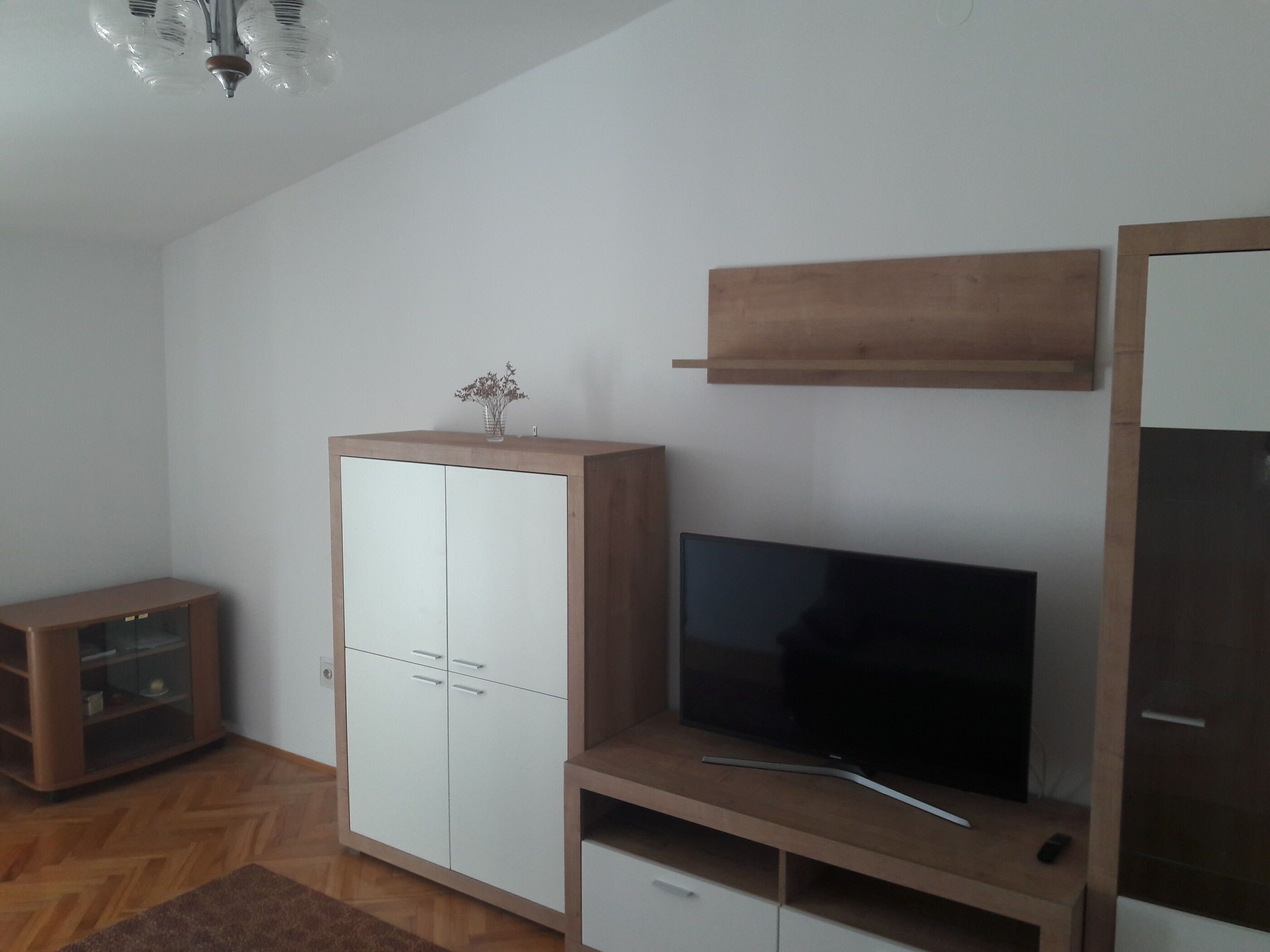 A room with a wooden cabinet, a television on a wooden stand, and a small cabinet with glass doors.