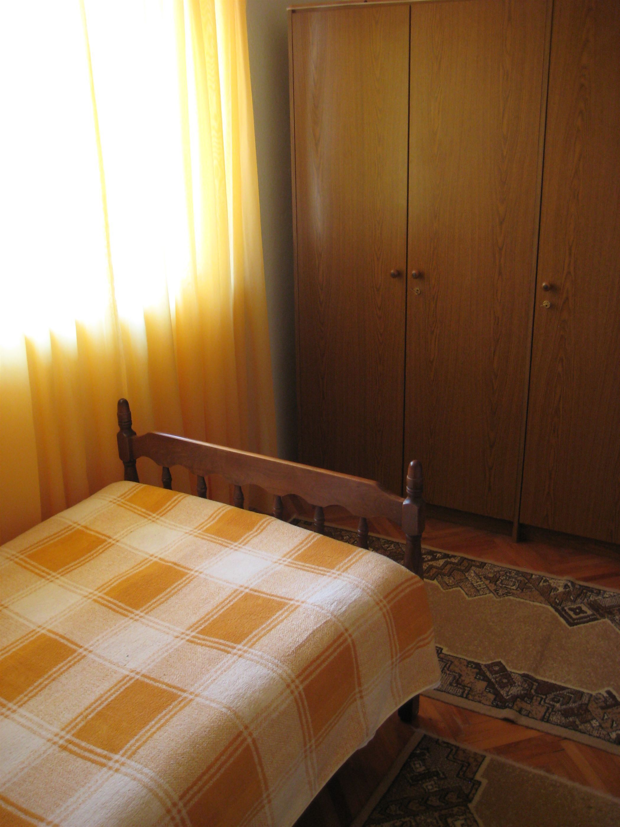 A room with a bed, a wooden wardrobe, and a patterned rug.