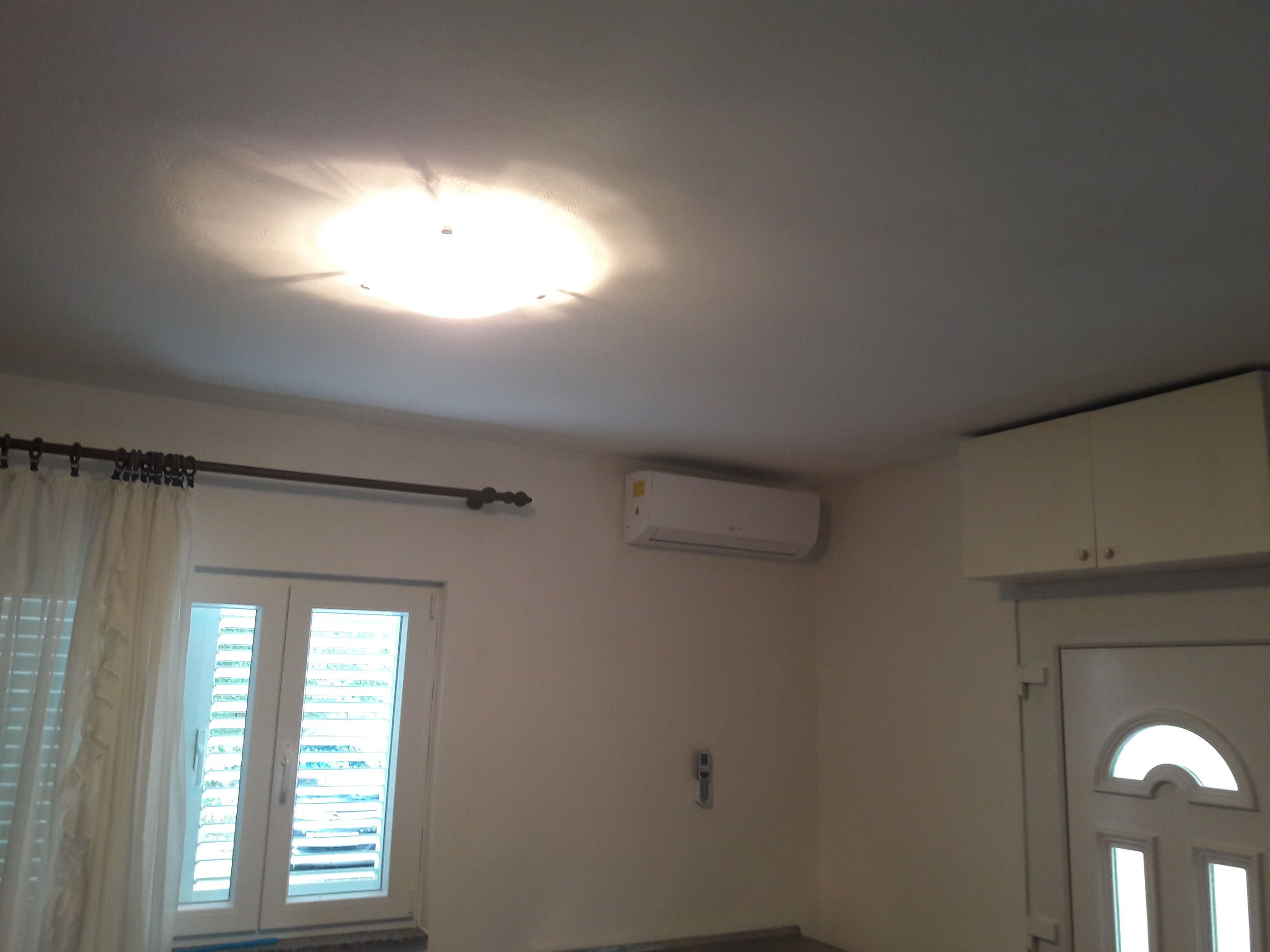 Une pièce dotée d’un luminaire au plafond, d’un appareil de climatisation, d’une fenêtre avec des stores et d’une porte surmontée d’une arche en demi-cercle.
