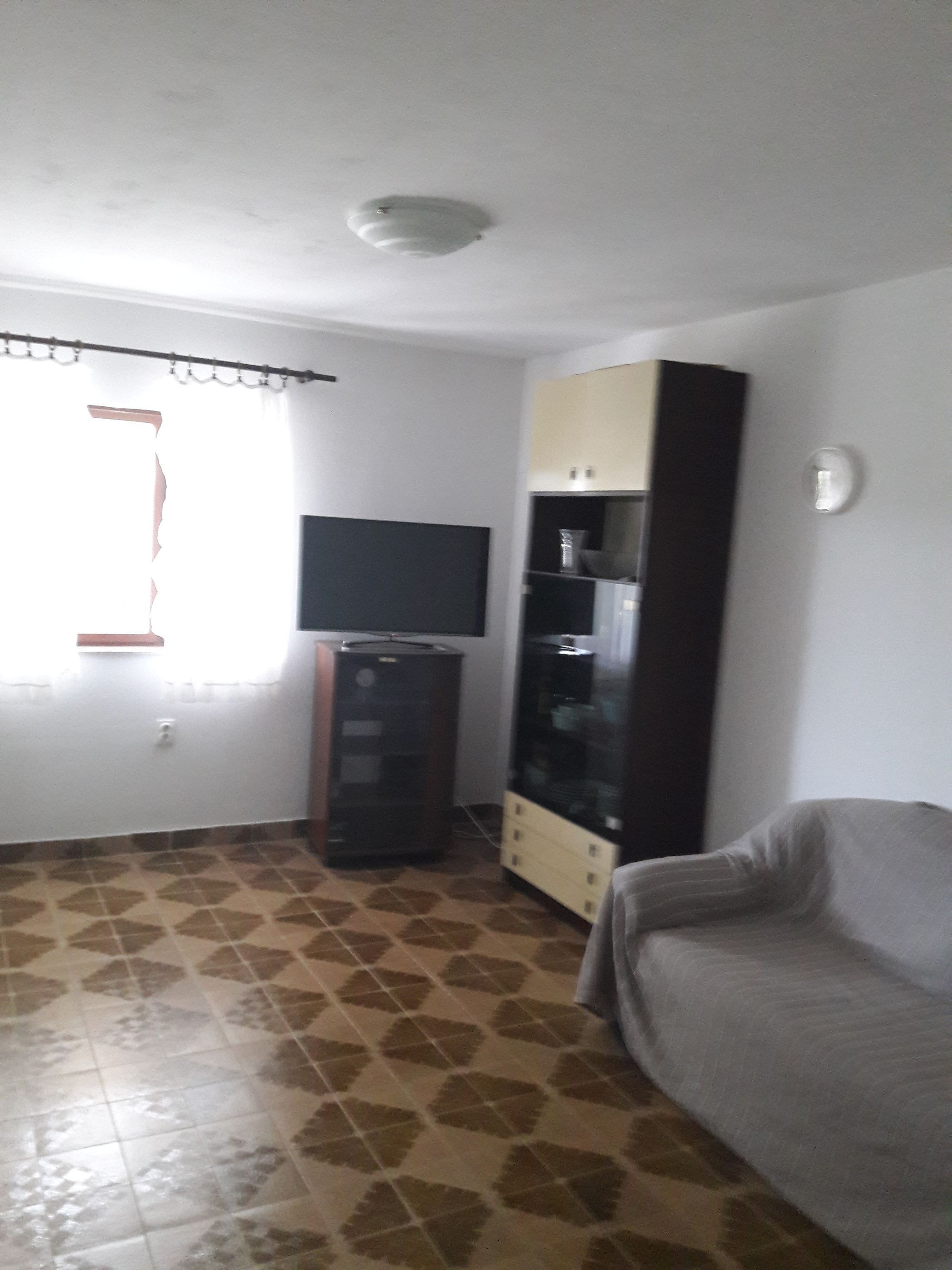 A living room with a sofa, a television on a stand, a cabinet, and patterned flooring.