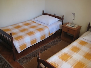 A small, single-bed room with a wooden bed frame, a nightstand with a lamp, and a patterned rug. - Apartments Biserka (Rogoznica)