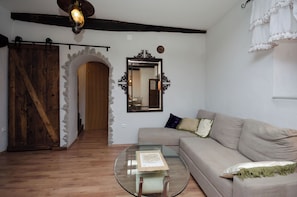 Ein Wohnzimmer mit einem Glastisch, einem beigen Sofa, einer Holztür und einem Steingewölbe.