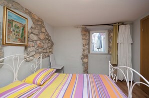 A bedroom with a bed, a chair, a window with curtains, and a stone wall. - Apartments Marija Ivan (Vrbnik)