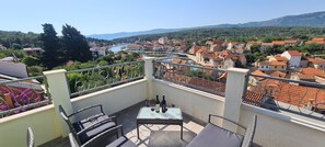 Un balcone con tavolo e sedie, affacciato su una città con un fiume e montagne sullo sfondo.