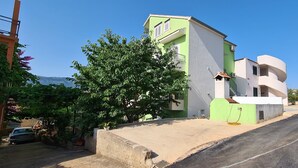 A residential building with a green and white facade, a concrete driveway, and a tree in front. - Apartment On the top (Jelsa)