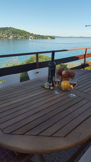 A wooden table with a bottle, glasses, and a bowl of fruit by a lakeside view. - Apartment Ana (Kali)