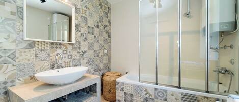 A bathroom with a white sink, a large mirror, a glass-enclosed shower, and patterned tiles.