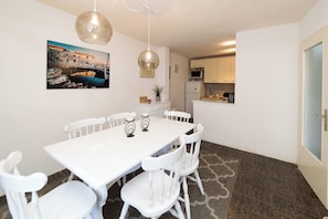 A dining area with a white table and chairs, a pendant light, a kitchen in the background, and a framed picture on the wall. - House Panorama House (Novi Vinodolski)