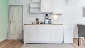 Eine kleine Küche mit weißen Schränken, einer Arbeitsfläche mit Kaffeemaschine, Toaster und kleinem Kühlschrank.