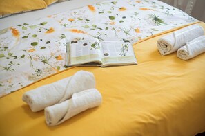 A bed with a floral bedspread, a book, and rolled towels. - Apartment Ivana (Sibenik)