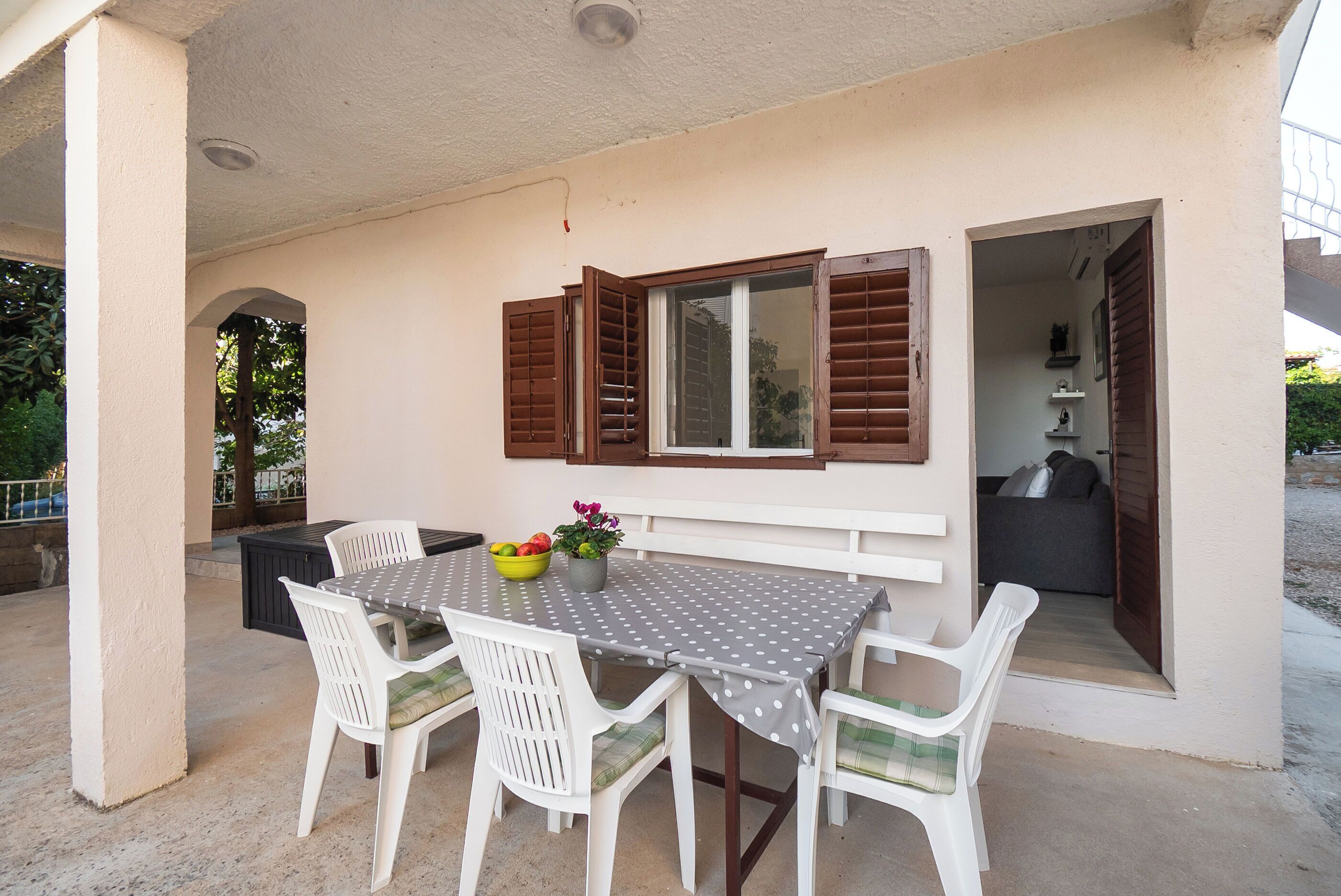 A covered patio with a table and chairs, a window with shutters, and a view into the house.