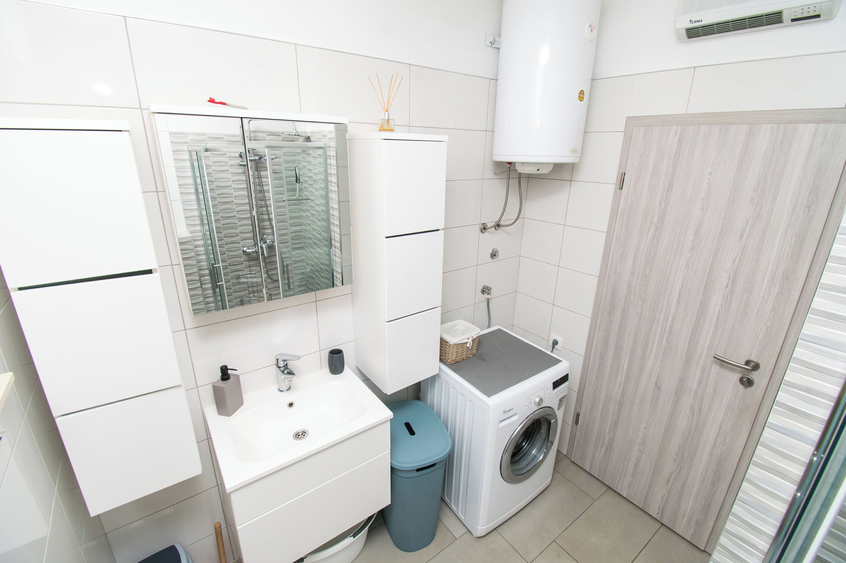A compact bathroom with a glass shower enclosure, a washing machine, and a sink.