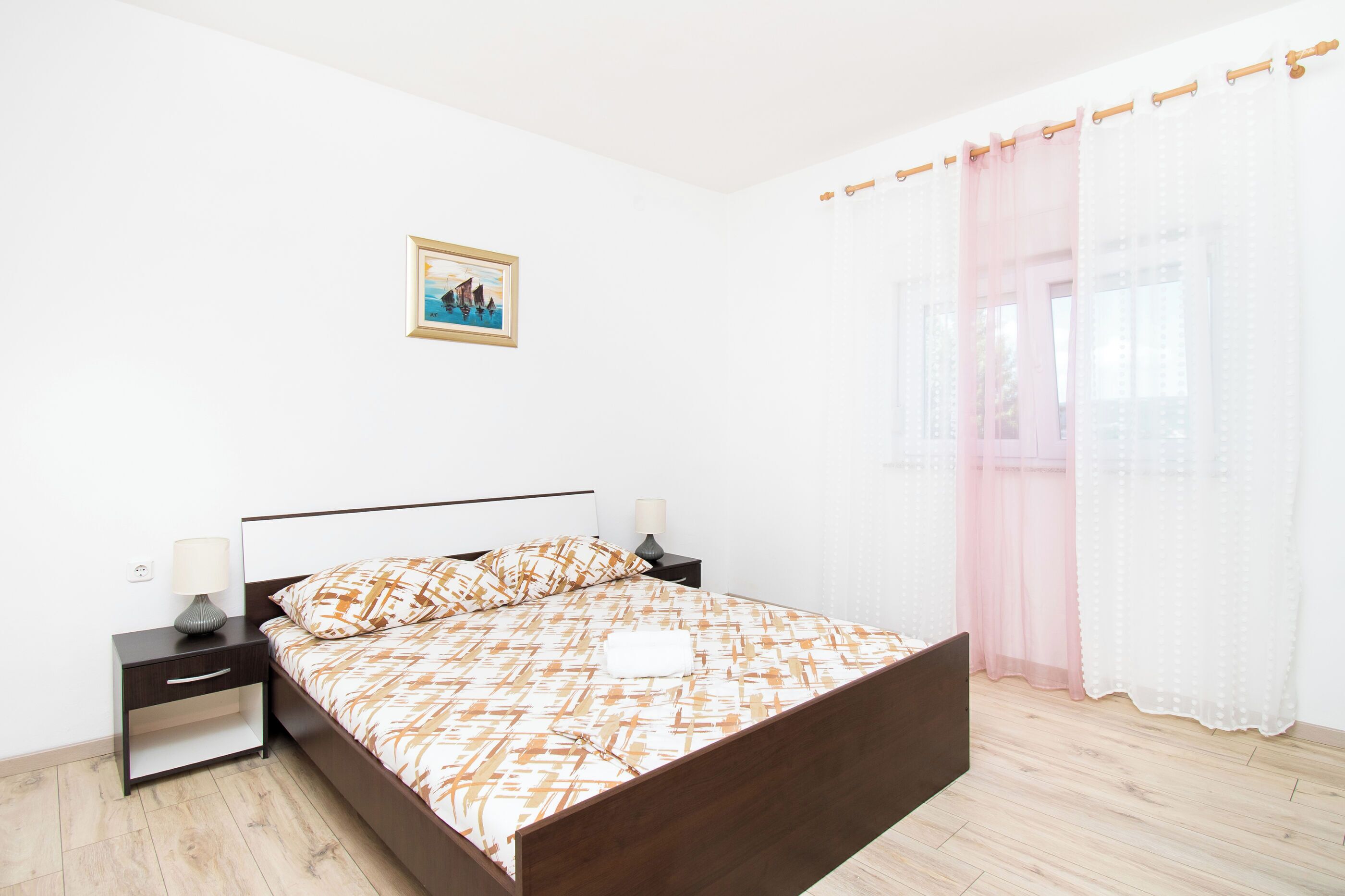 A bedroom with a bed, nightstands, a picture on the wall, and sheer curtains.