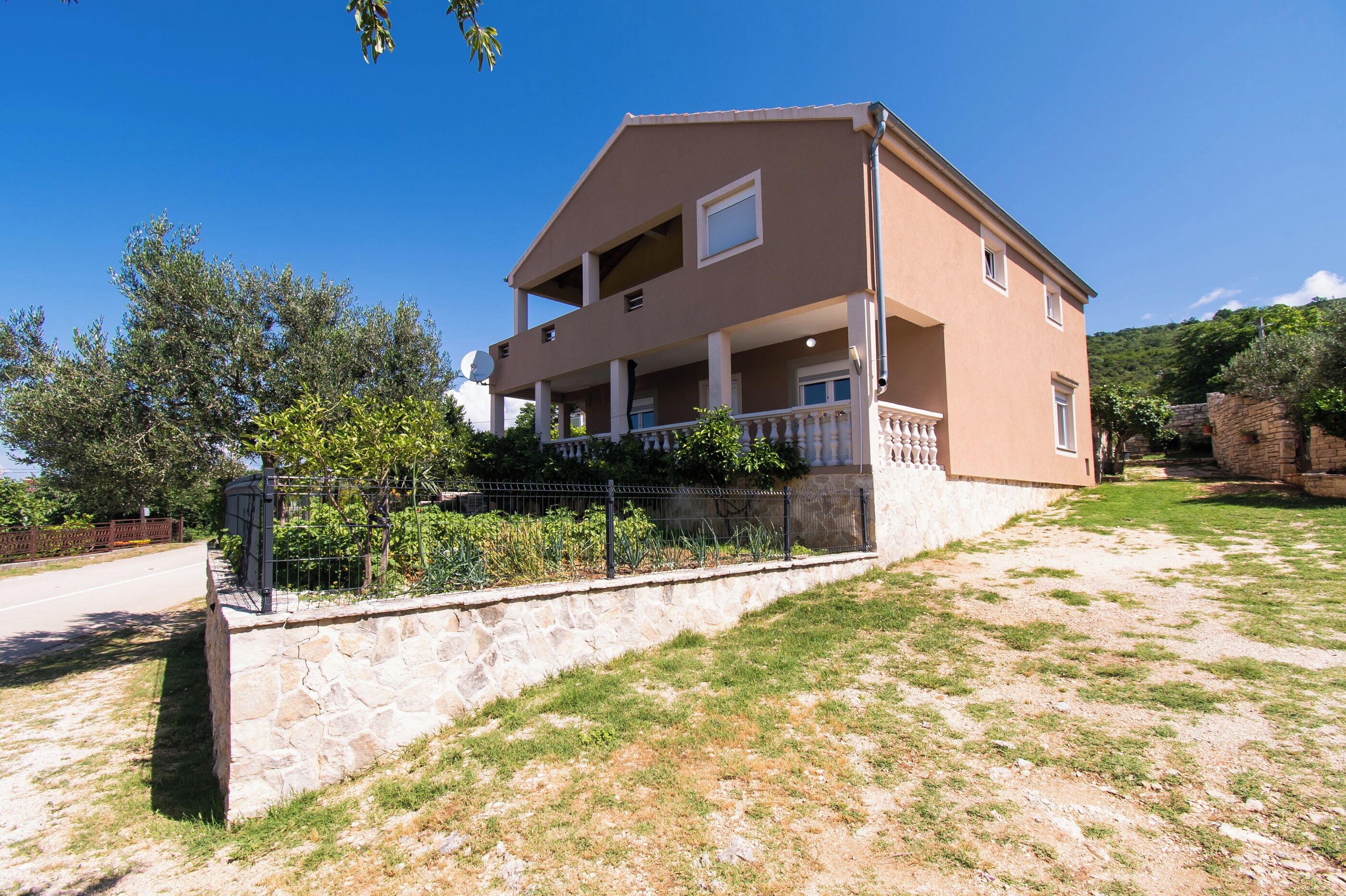 A two-story house with a stone foundation, a balcony, and a garden area.
