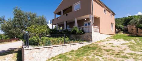 A two-story house with a stone foundation, a balcony, and a garden area.