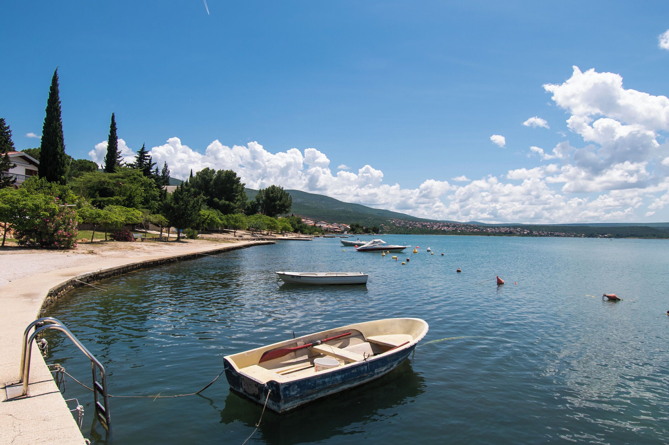 A calm lake with boats, a dock, and a mountainous landscape in the background.
