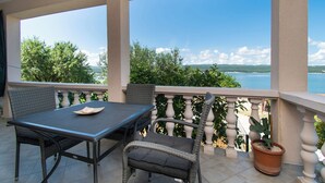 A balcony with a table and chairs, a potted plant, and a view of the sea and greenery. - House Sea and River (Obrovac)
