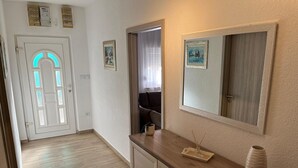 A hallway with a wooden floor, a white door with a blue light, a mirror, and a small table with a vase and candle. - House Sea and River (Obrovac)
