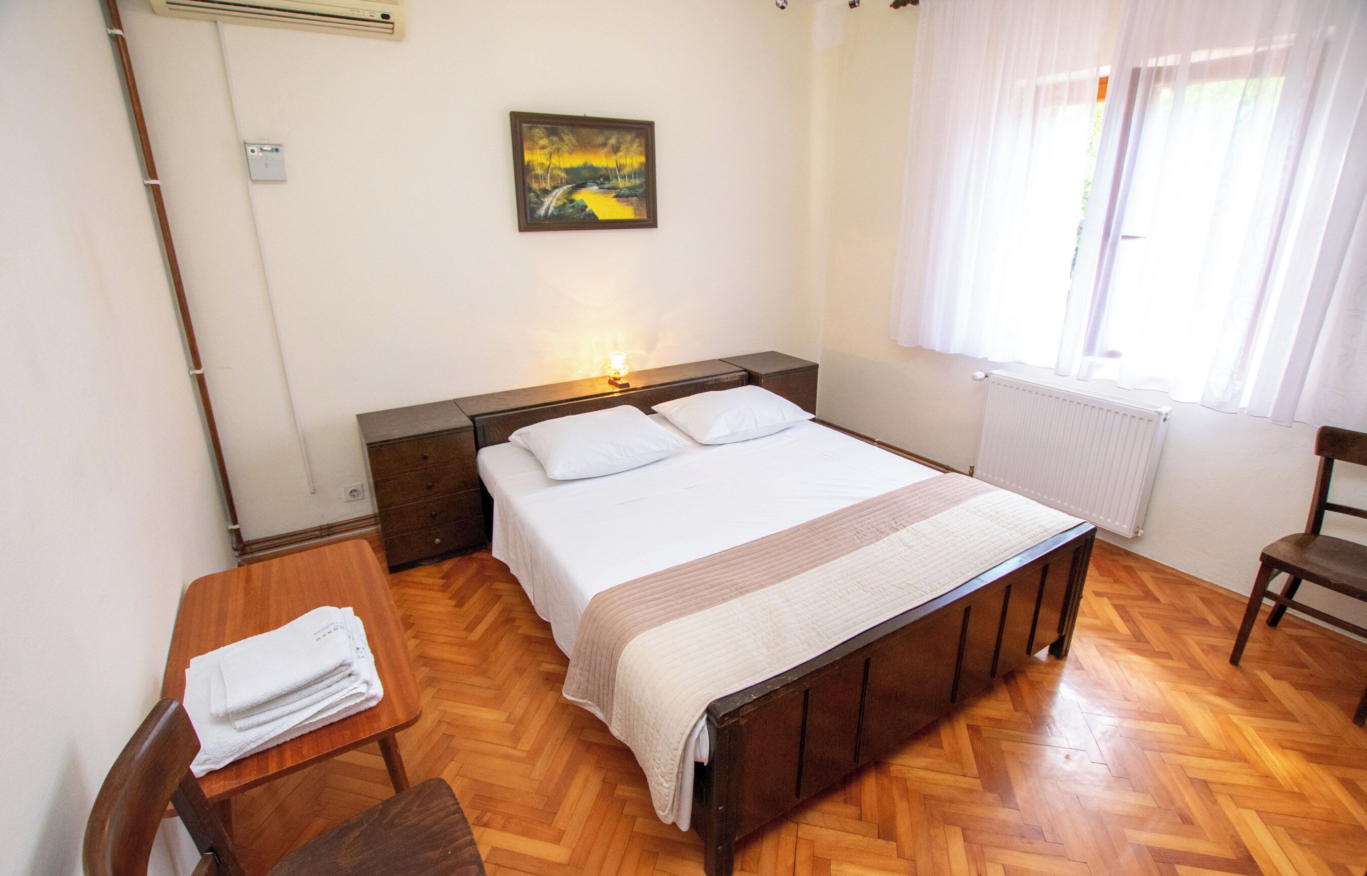 Une chambre à coucher avec un lit en bois, une table de chevet avec une lampe, une chaise et un tableau accroché au mur.