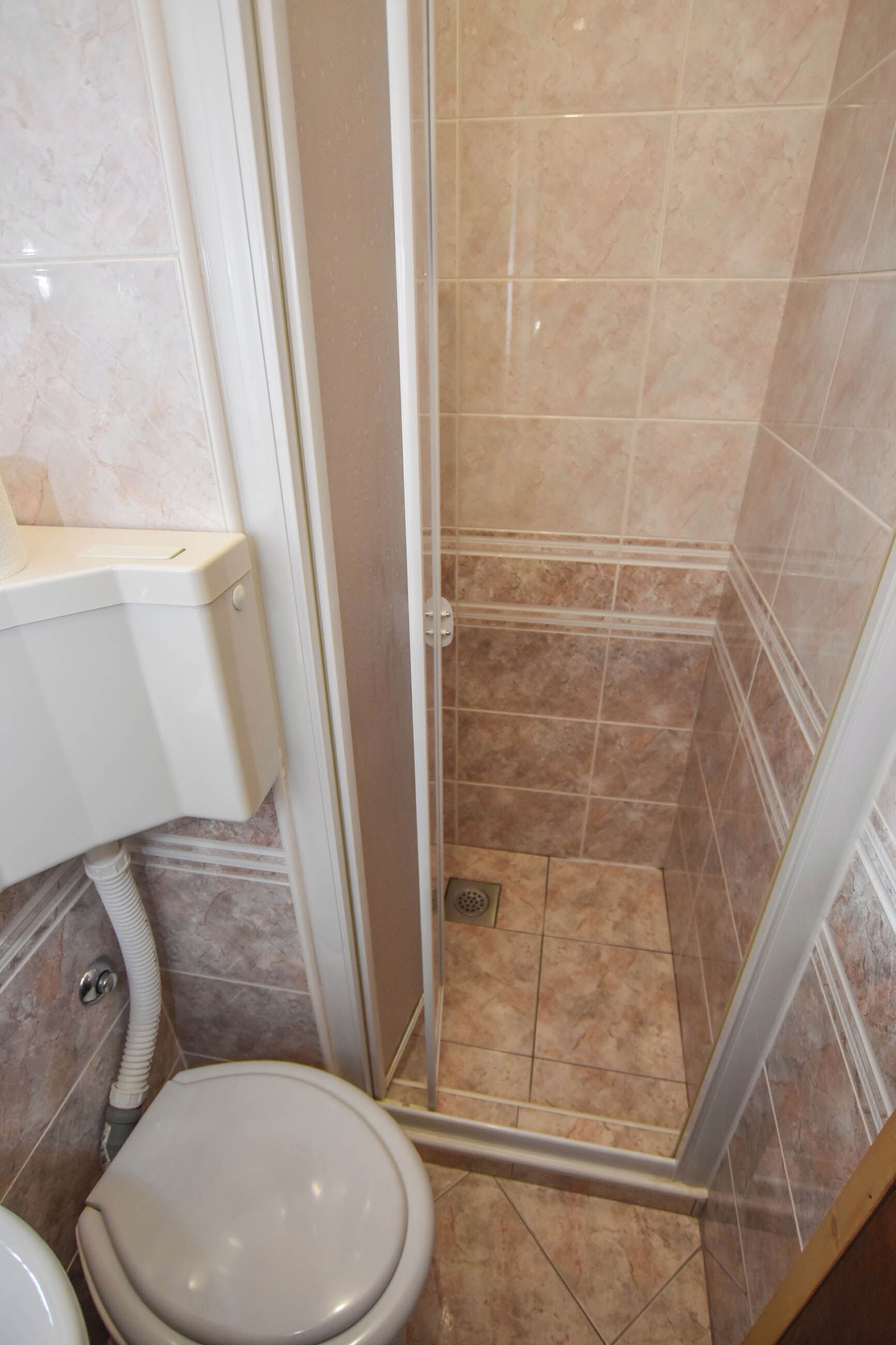 A bathroom with a toilet, a shower enclosure, and a toilet paper holder.