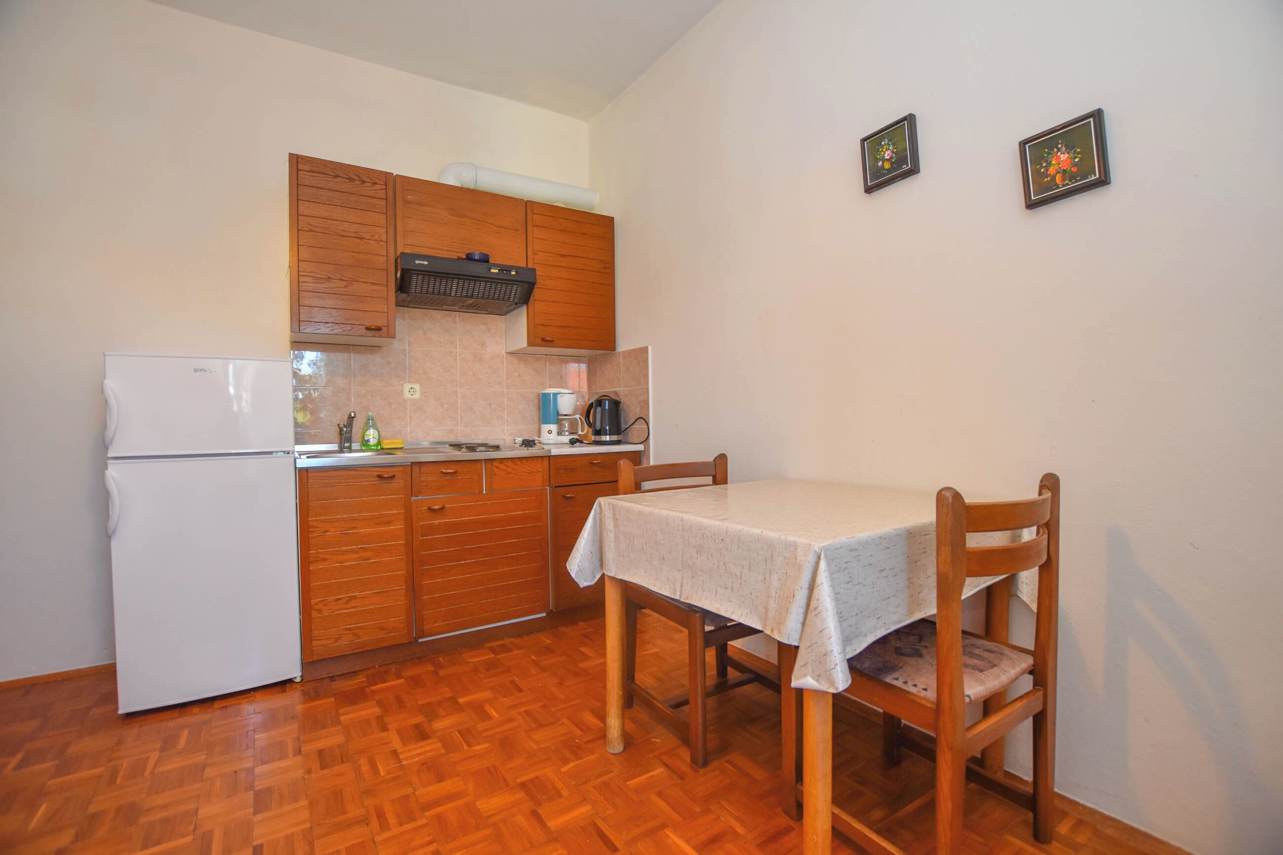 Cocina compacta con armarios de madera, un refrigerador blanco, una mesa de comedor con sillas y dos cuadros en la pared.
