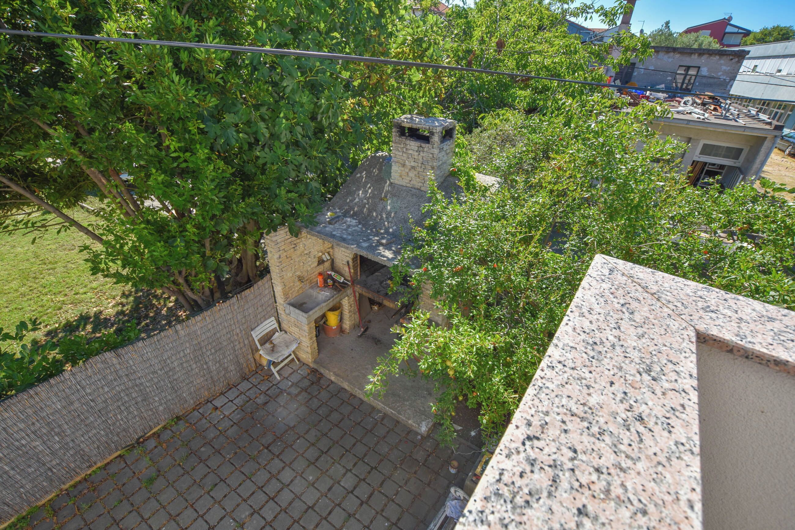 A small brick building with a chimney, surrounded by lush green trees.