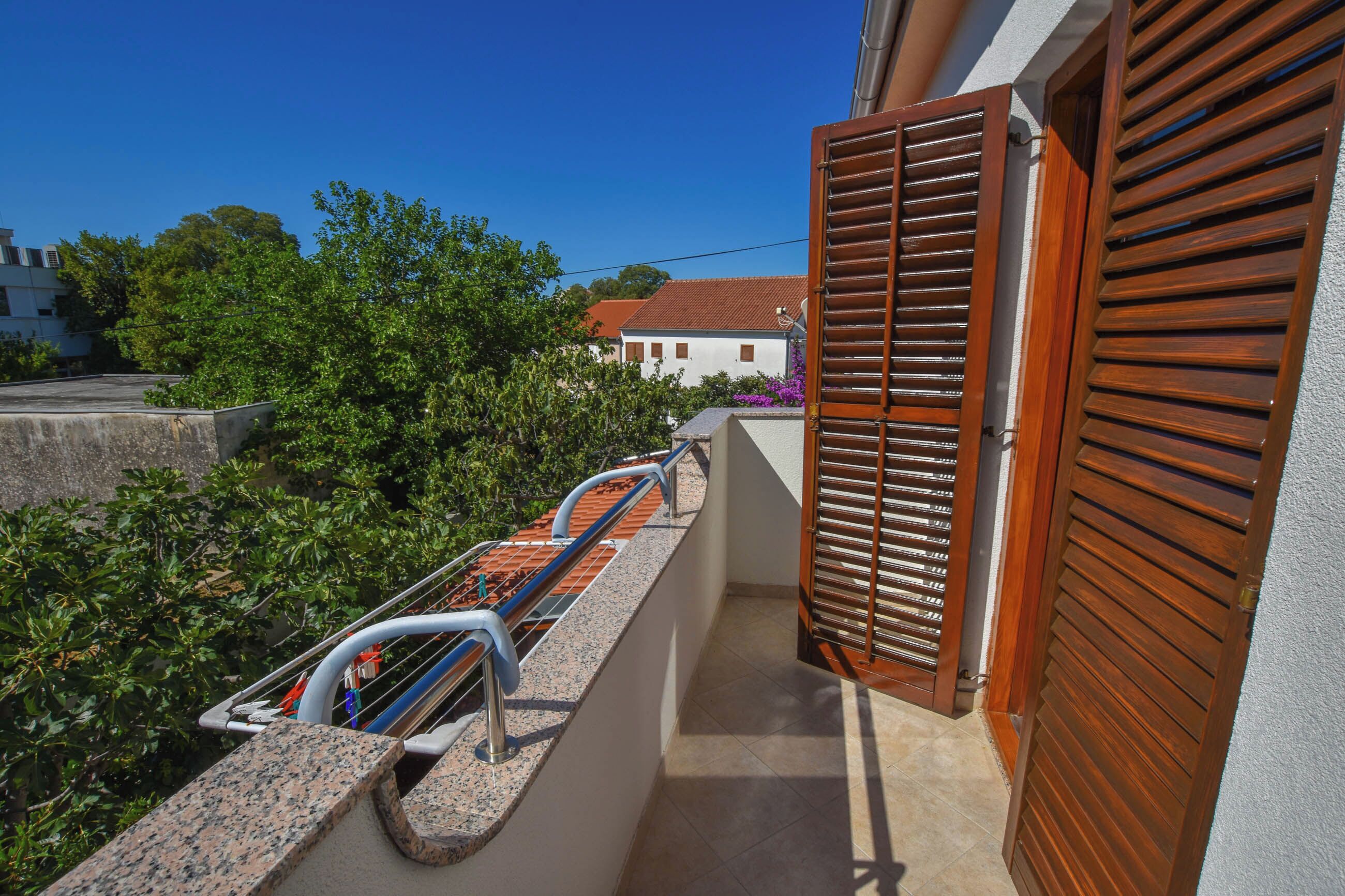 A balcony with a metal railing, a wooden door, and a view of a house with a red roof.