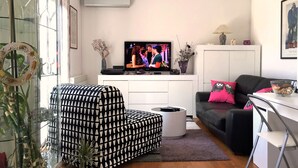 A modern living room with a black and white patterned sofa, a black couch with pink pillows, a glass coffee table, and a television on a white cabinet. - Apartment Ivana With Jacuzzi (Vir)