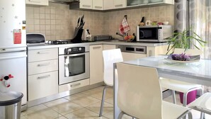 A modern kitchen with white cabinets, a gas stove, an oven, a microwave, and a dining area with a glass table and white chairs. - Apartment Ivana With Jacuzzi (Vir)