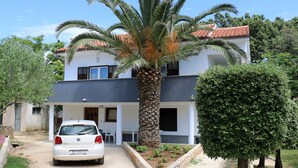 A two-story building with a white facade and a red-tiled roof. A white car is parked in front. - Apartment Ivana With Jacuzzi (Vir)