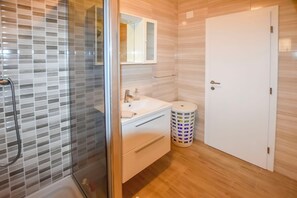 Une salle de bain moderne avec une douche à parois de verre, un lavabo blanc avec un miroir au-dessus, et une porte blanche.