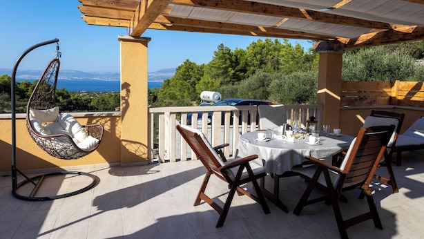 Un patio con una sedia a dondolo, sedie in legno, un tavolo apparecchiato per mangiare e vista sul mare.