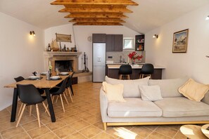 Et moderne køkken med indbygget køleskab, et spiseområde med et træbord og stole, samt en stue med sofa og puder.