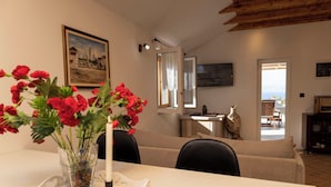 Zona pranzo con tavolo, sedie, un vaso con fiori rossi, una candela e un quadro appeso al muro.
