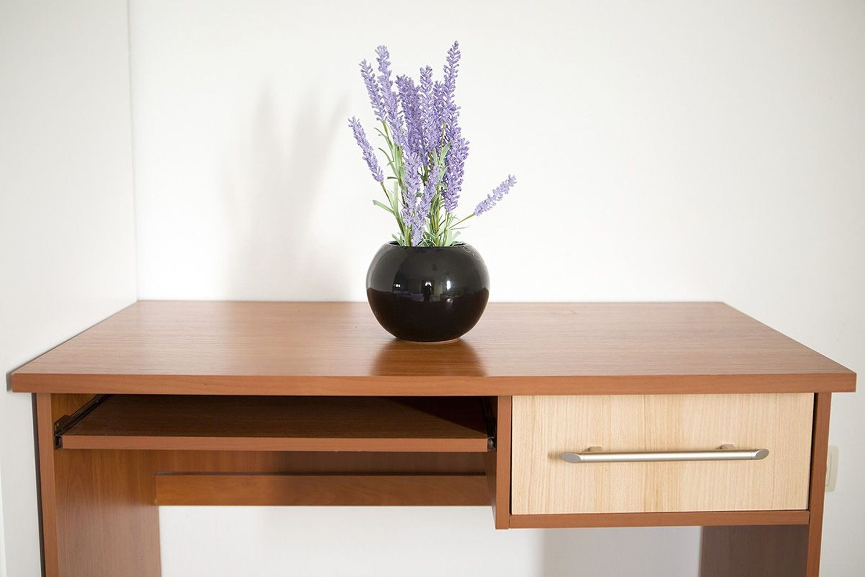 A wooden desk with a black vase containing lavender flowers.