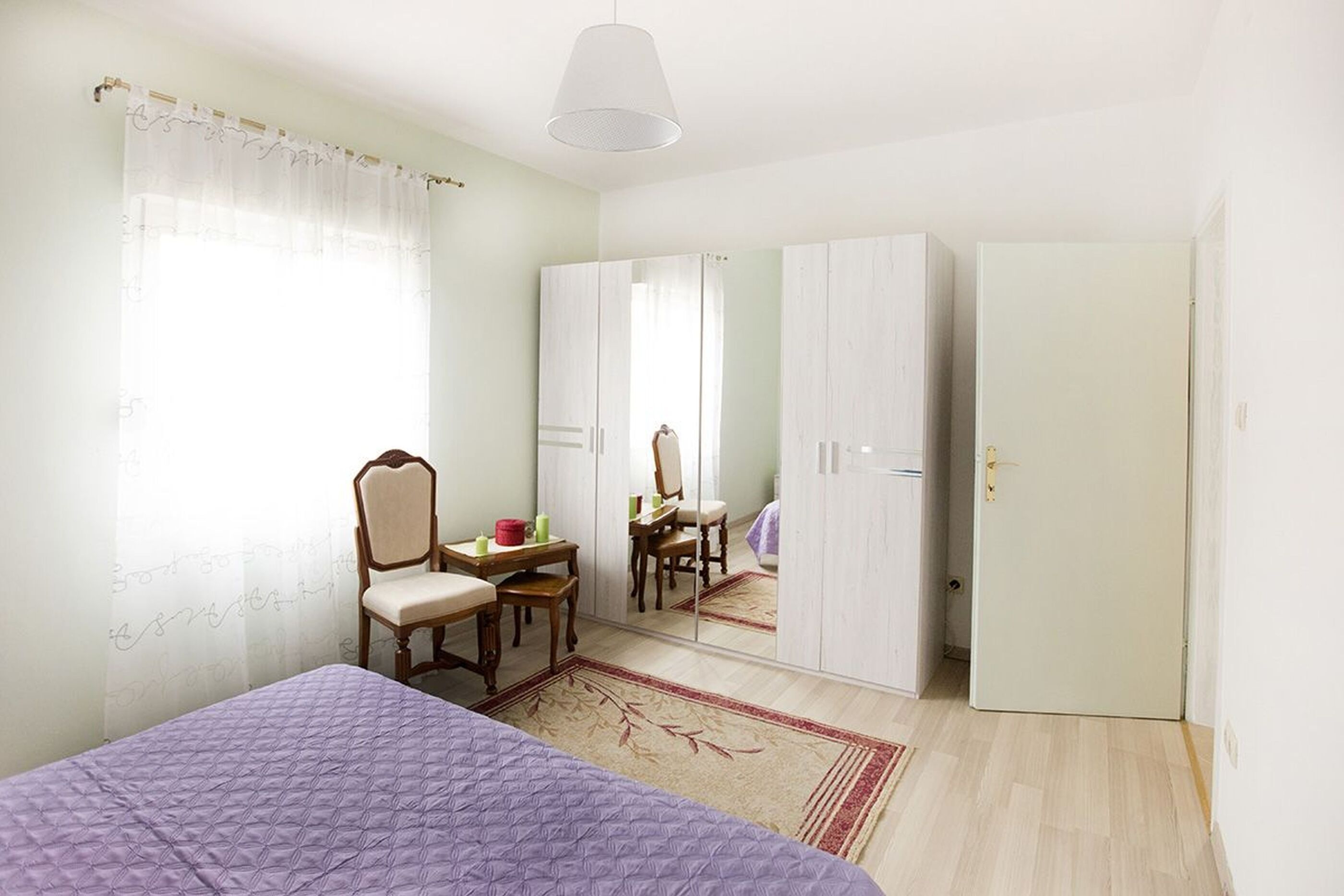 Un dormitorio con cama, escritorio, silla, armario y espejo.