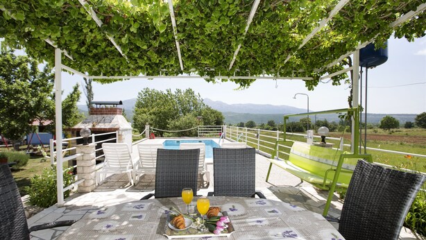 Ein überdachter Außenbereich mit Tisch für zwei Personen, mit Blick auf Pool und Berge.
