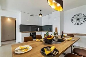 A modern kitchen with white cabinets, a black countertop, and a large clock on the wall. - Villa Three Units (Crikvenica)