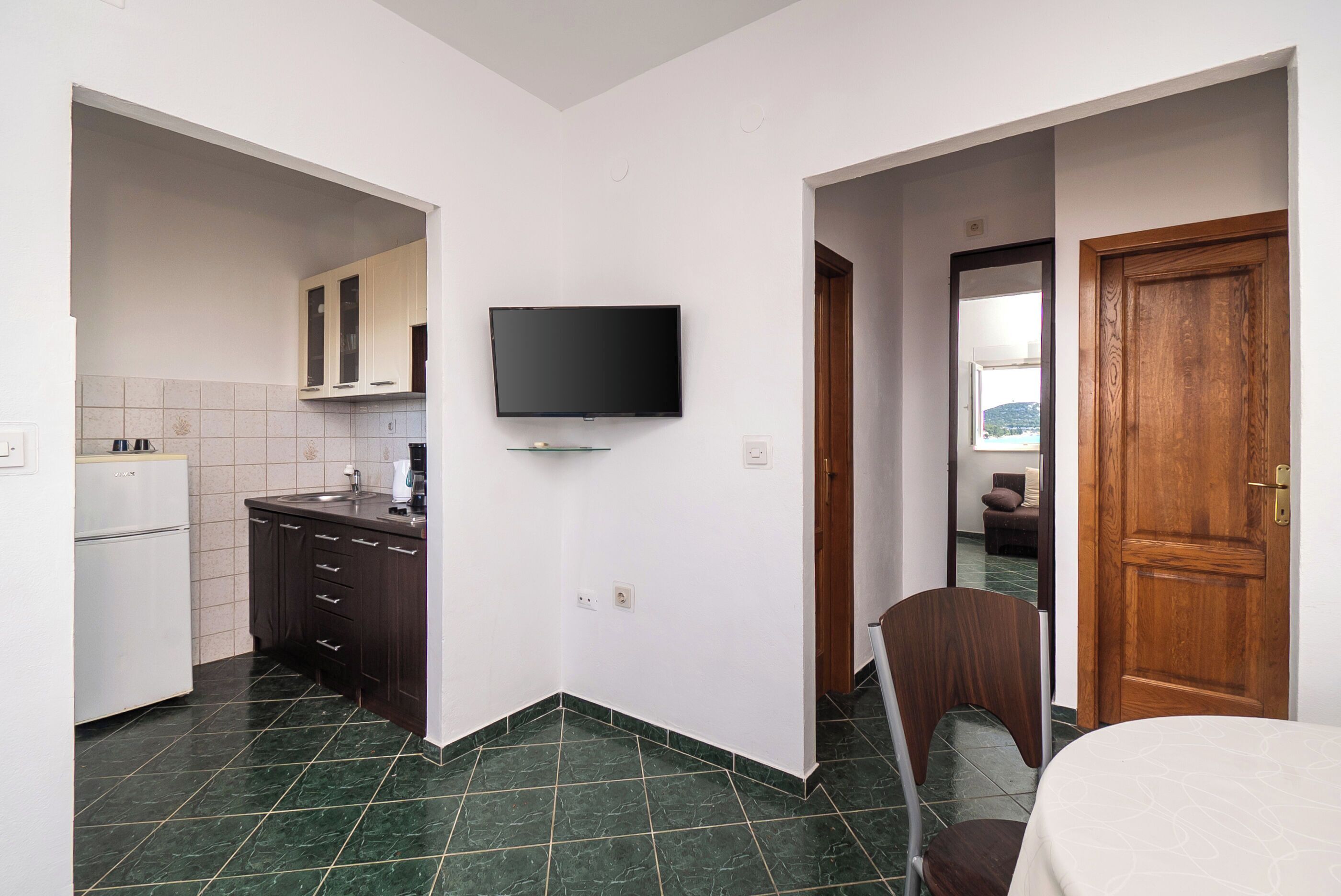 A compact kitchen with a TV, a refrigerator, and a wooden door.