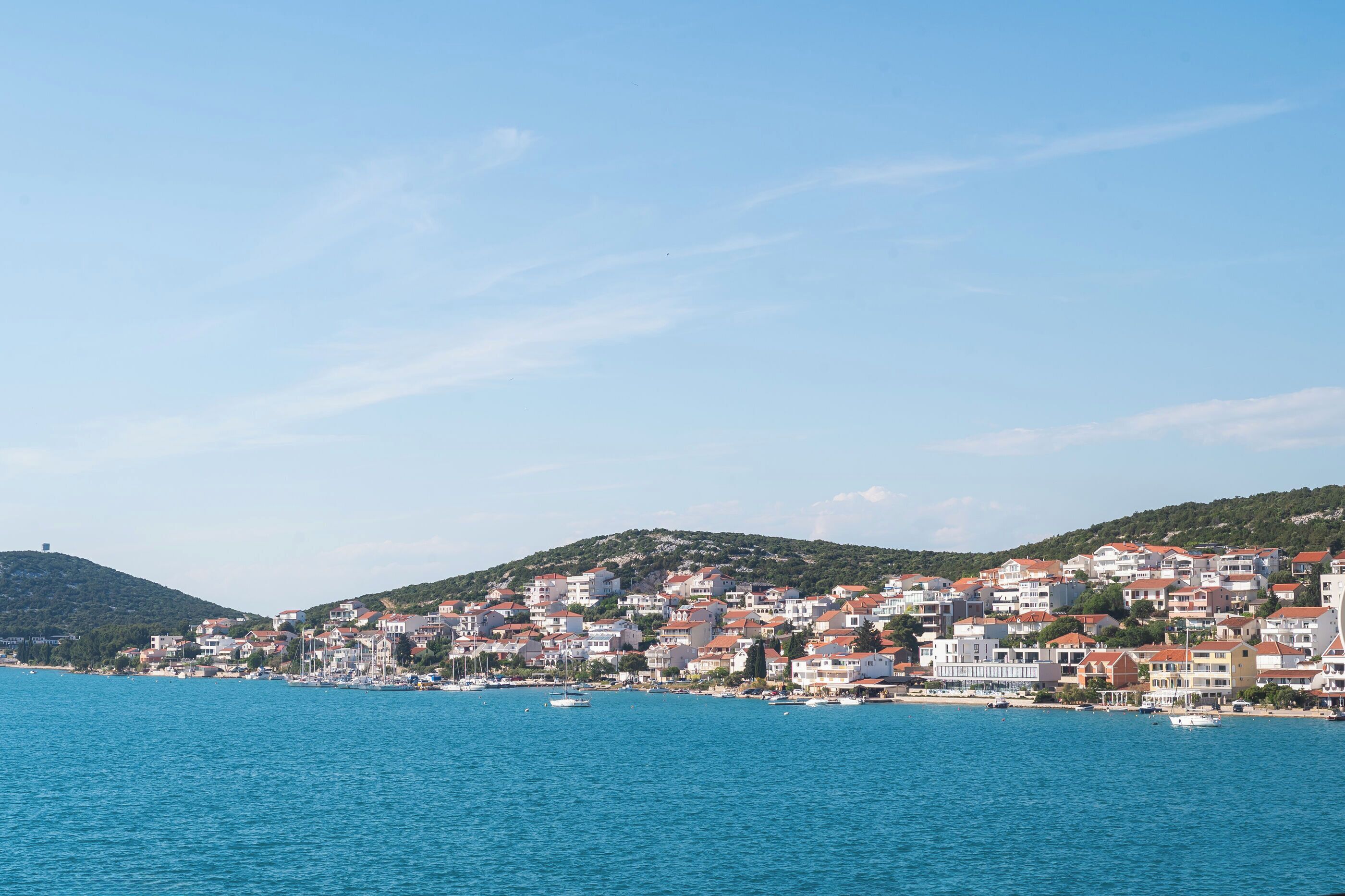 A coastal town with buildings along the waterfront, boats in the water, and hills in the background.