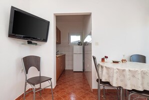 Eine kleine Küche mit einem an der Wand montierten Fernseher, einem Esstisch mit Stühlen und einem Fenster über der Spüle.