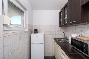 A compact kitchen with a refrigerator, microwave, sink, and wooden countertop. - Apartments Branko (Tisno)