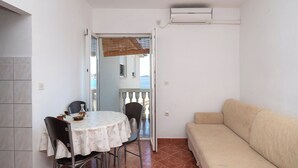 Une petite pièce comprenant une table à manger, des chaises, un canapé et une vue sur l’extérieur par une porte ouverte.