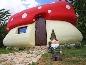 Une maison en forme de champignon, avec une porte et une statuette de gnome devant.