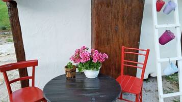 A round table with two red chairs, a white pot with pink flowers, and a wooden board leaning against a white wall.