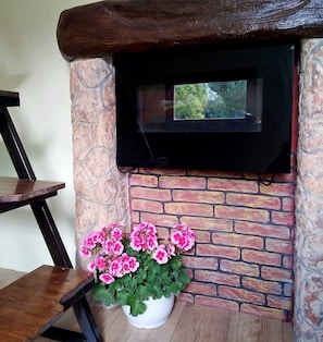 A stone fireplace with a black screen, a wooden table, and pink flowers in a white pot. - House Fairytale Village Castle (Skradin)