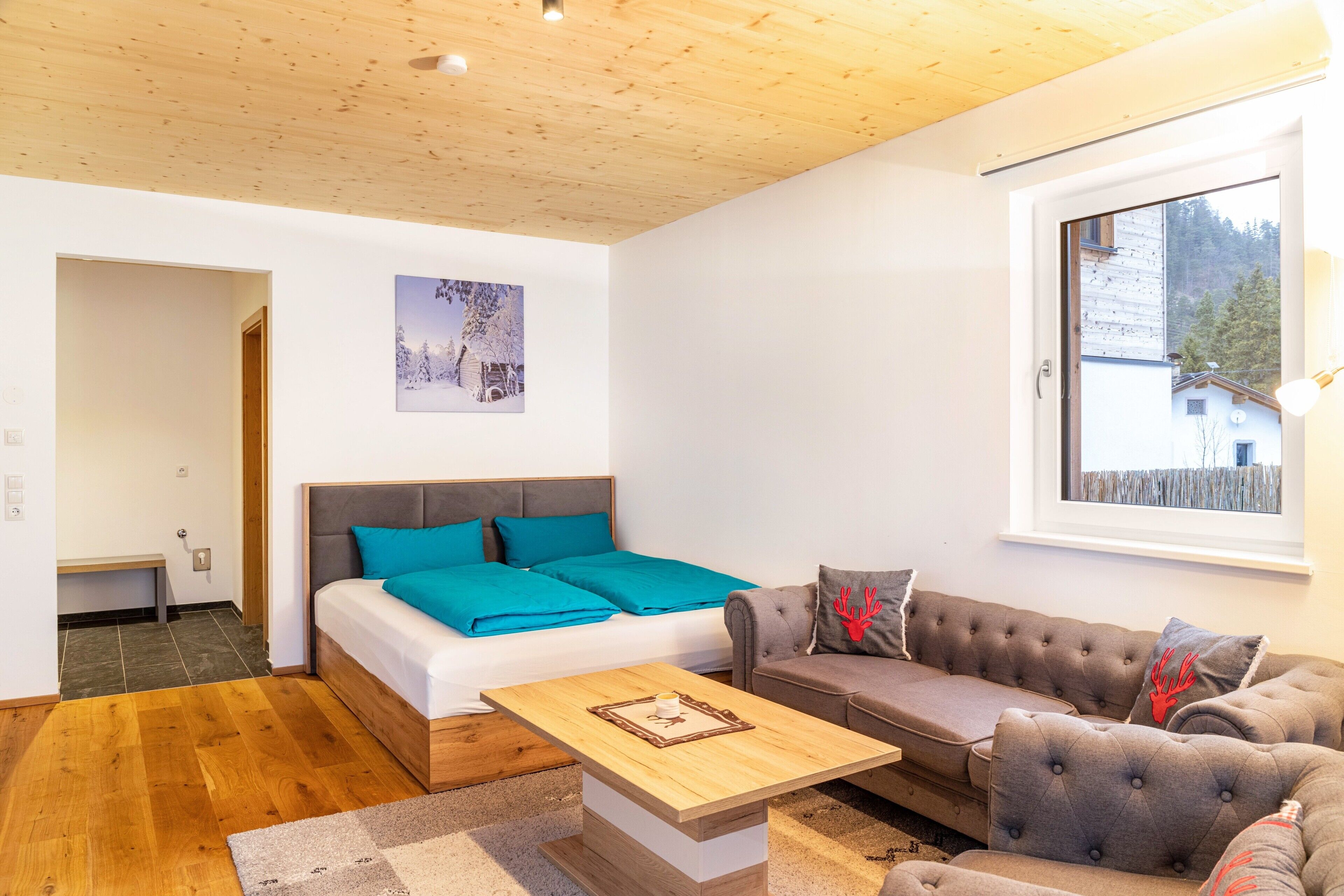 Una habitación moderna con cama, sofá y ventana con vista a edificios y árboles.