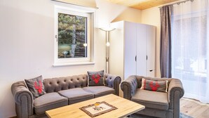 Una sala de estar acogedora con un sofá gris, una mesa de centro de madera y un ventanal con vistas a árboles.
