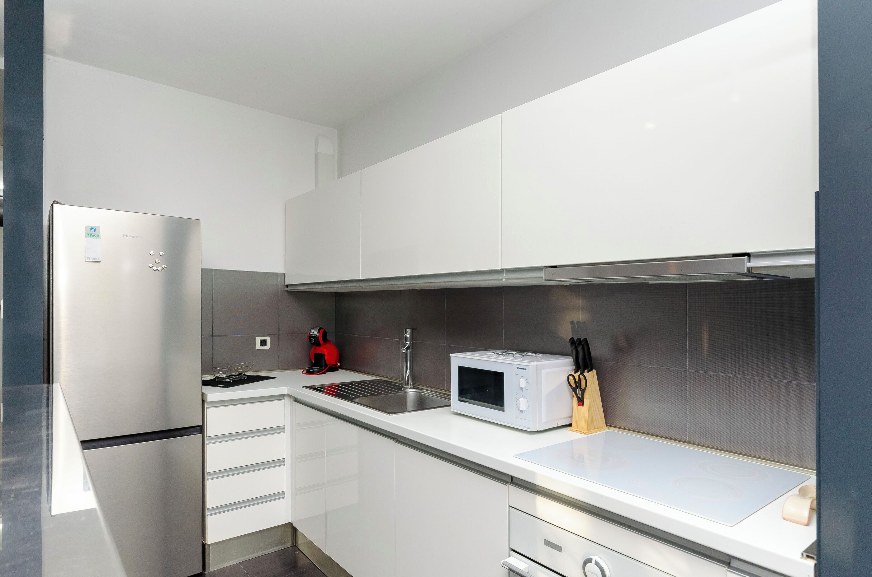 Una cucina moderna con mobili bianchi, un frigorifero in acciaio inox, un forno a microonde e un lavello.